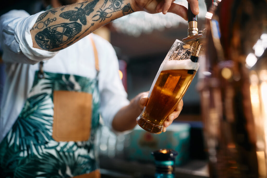 Close-up of bartender pouring draft beer in a glass while working in a bar.